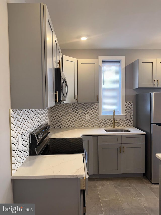 kitchen with appliances with stainless steel finishes, backsplash, gray cabinets, and sink