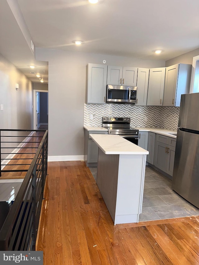 kitchen featuring appliances with stainless steel finishes, backsplash, gray cabinetry, and light wood-type flooring