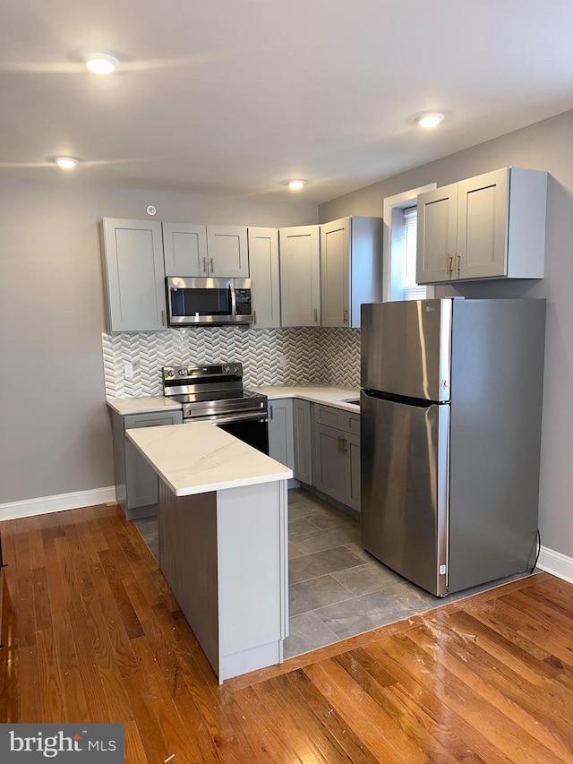 kitchen with appliances with stainless steel finishes, gray cabinetry, light stone counters, and dark hardwood / wood-style flooring