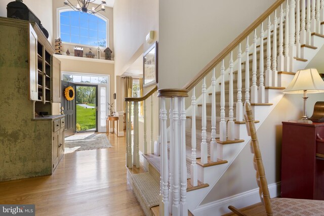 foyer entrance with an inviting chandelier, a towering ceiling, and light hardwood / wood-style flooring