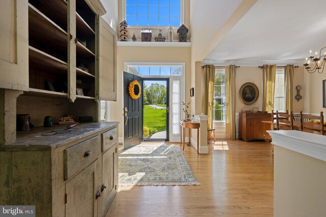 foyer entrance featuring crown molding, a towering ceiling, light hardwood / wood-style flooring, and a notable chandelier