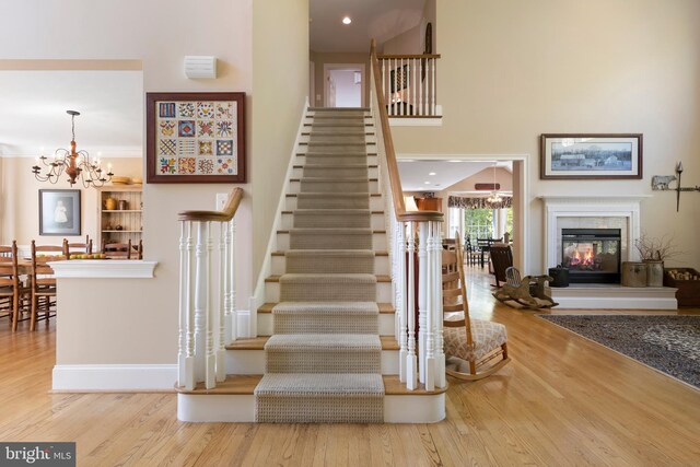 staircase with hardwood / wood-style flooring, a multi sided fireplace, a towering ceiling, and a notable chandelier