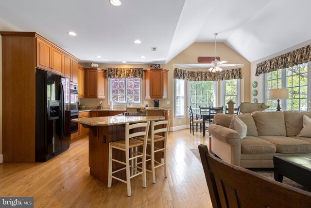 kitchen featuring vaulted ceiling, a kitchen bar, light hardwood / wood-style floors, a kitchen island, and black refrigerator with ice dispenser