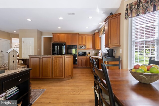 kitchen with light stone counters, light hardwood / wood-style floors, a kitchen island, and black appliances