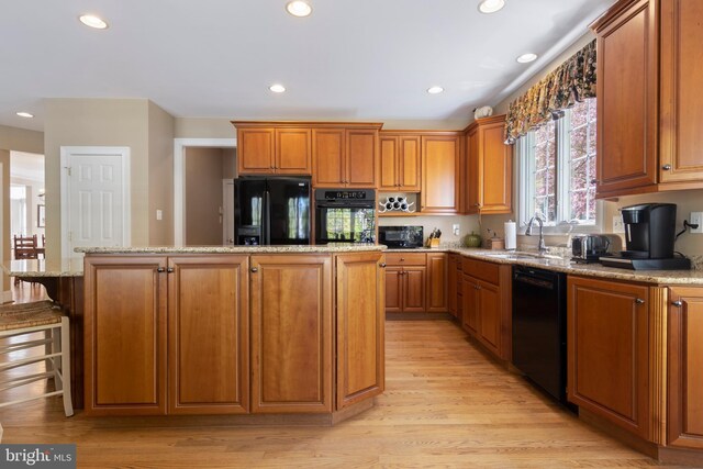 kitchen featuring light stone countertops, sink, a kitchen island, and black appliances