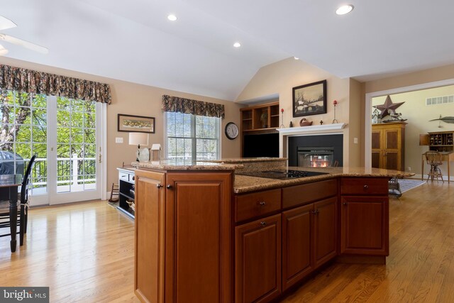 kitchen featuring light stone counters, lofted ceiling, a center island, and light hardwood / wood-style flooring