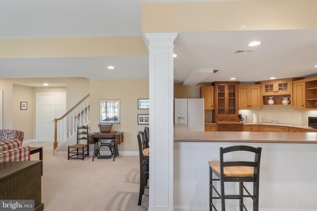 kitchen featuring a breakfast bar, kitchen peninsula, light colored carpet, white refrigerator with ice dispenser, and decorative columns