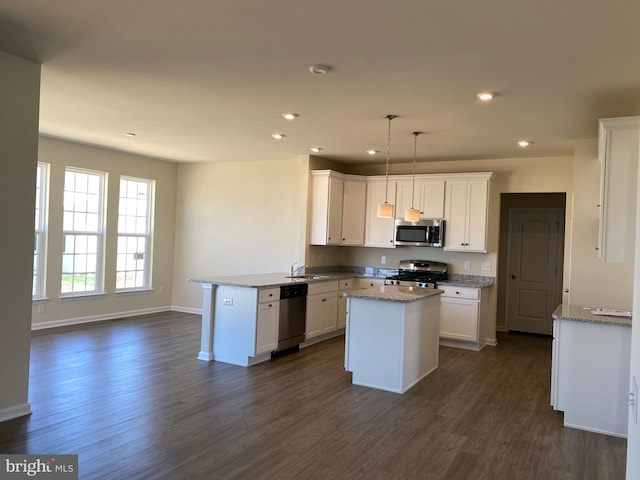 kitchen with appliances with stainless steel finishes, white cabinetry, sink, hanging light fixtures, and light stone counters