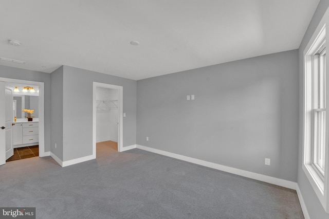 unfurnished bedroom with a closet, dark carpet, a spacious closet, and multiple windows