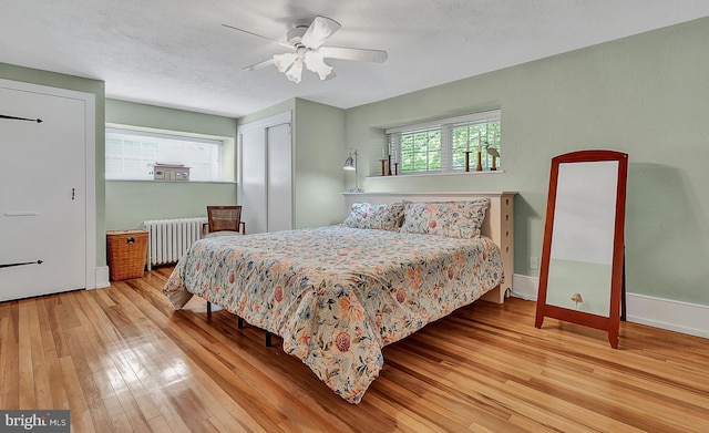 bedroom with radiator heating unit, ceiling fan, a closet, and light wood-type flooring