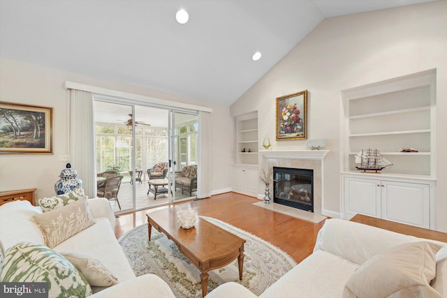 living room with built in shelves, ceiling fan, a premium fireplace, light hardwood / wood-style flooring, and vaulted ceiling