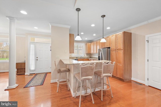 kitchen with a kitchen breakfast bar, light stone counters, stainless steel refrigerator with ice dispenser, decorative columns, and kitchen peninsula