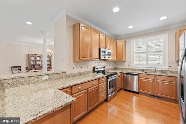 kitchen with sink, an inviting chandelier, light stone counters, appliances with stainless steel finishes, and light wood-type flooring