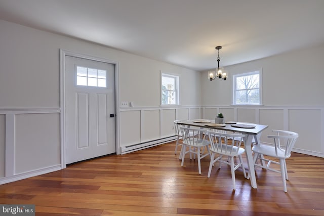 dining space featuring a notable chandelier, a baseboard radiator, a healthy amount of sunlight, and wood-type flooring