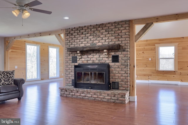 living room featuring vaulted ceiling with beams, ceiling fan, dark wood-type flooring, a brick fireplace, and wooden walls