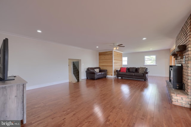 unfurnished living room with dark wood-type flooring, ceiling fan, a wood stove, a brick fireplace, and crown molding