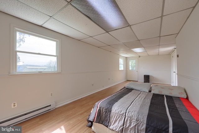 unfurnished bedroom featuring light hardwood / wood-style flooring, a drop ceiling, a baseboard heating unit, and multiple windows