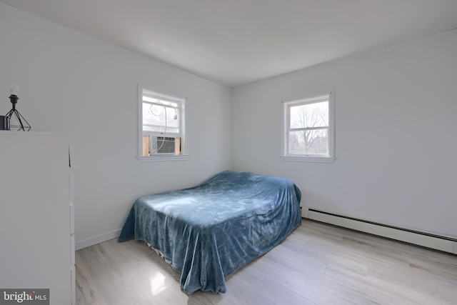 bedroom featuring light hardwood / wood-style flooring, a baseboard heating unit, and multiple windows