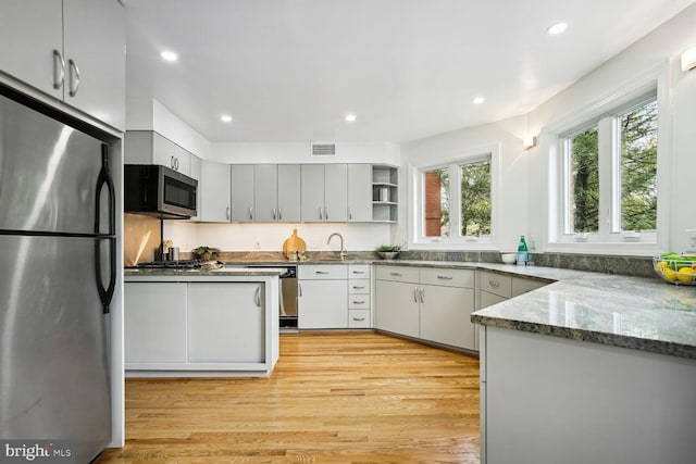 kitchen with sink, light hardwood / wood-style flooring, stainless steel appliances, dark stone counters, and gray cabinets