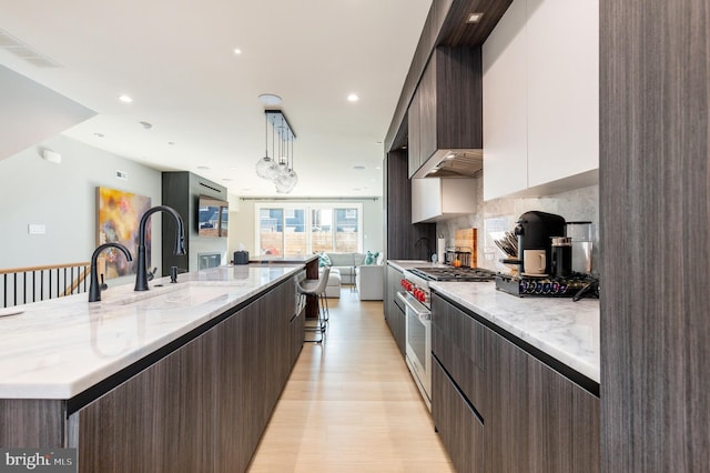 kitchen with high end range, a large island with sink, a sink, dark brown cabinets, and modern cabinets