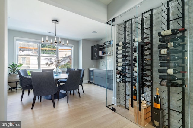 wine area featuring beverage cooler, light wood-type flooring, and a chandelier