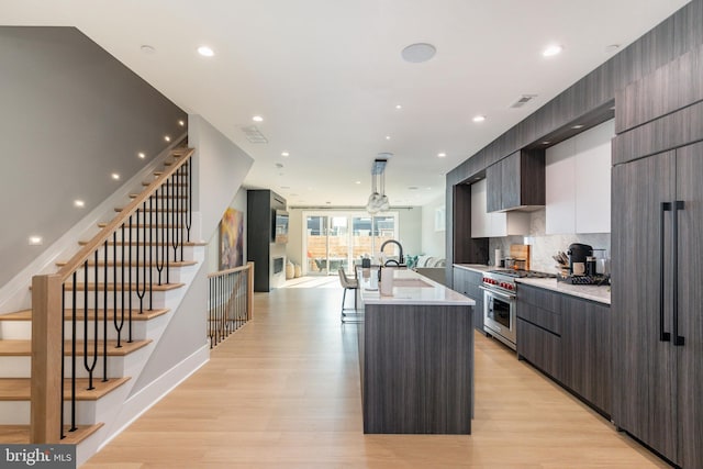 kitchen featuring premium appliances, an island with sink, light hardwood / wood-style floors, decorative backsplash, and white cabinets