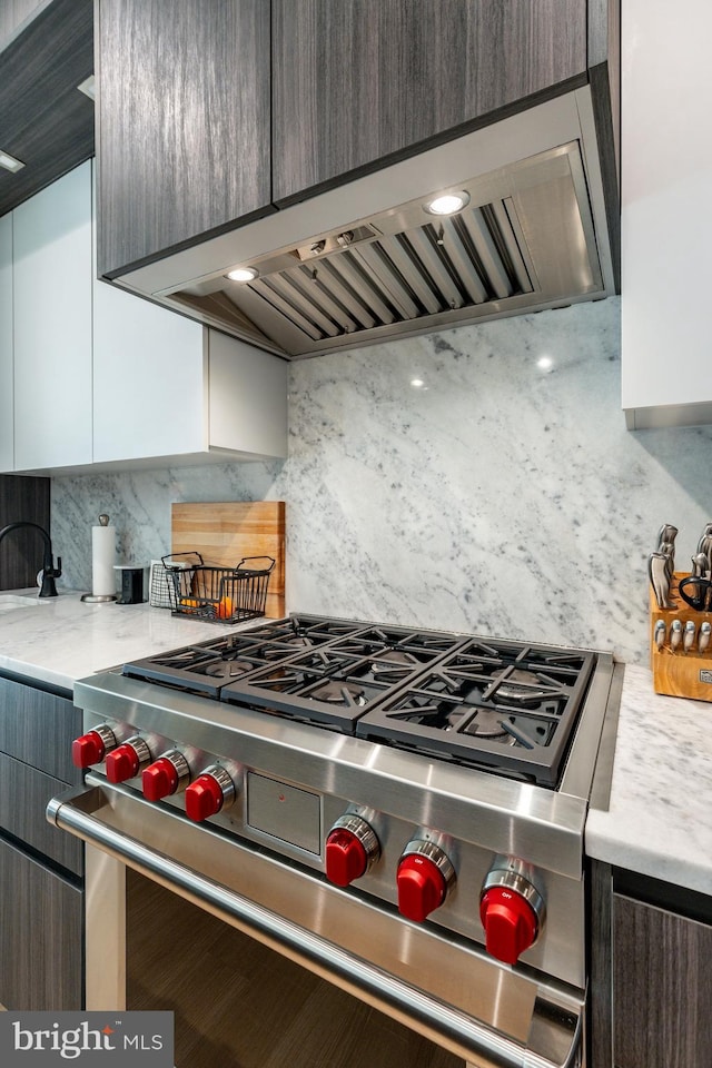 kitchen with decorative backsplash, light stone countertops, exhaust hood, and stainless steel range