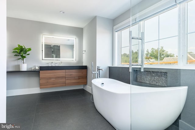 bathroom featuring tile patterned floors, a freestanding tub, baseboards, and vanity