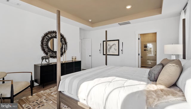 bedroom featuring ensuite bath, a tray ceiling, and dark wood-type flooring