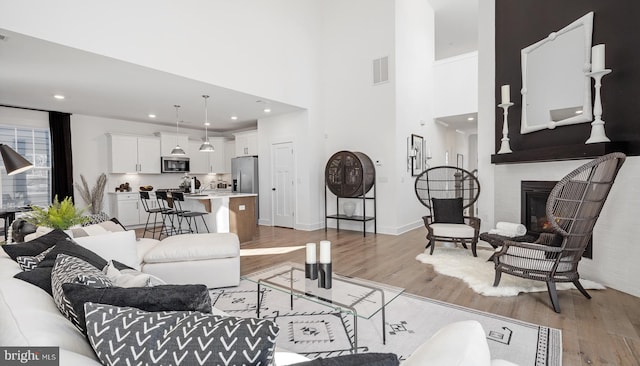 living room with light hardwood / wood-style floors, a brick fireplace, and a high ceiling