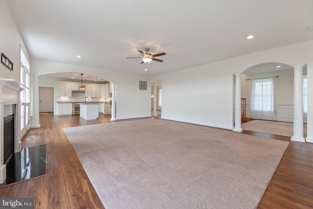 unfurnished living room featuring carpet floors, sink, ceiling fan, and ornate columns