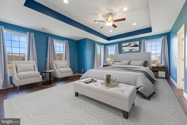 bedroom featuring a raised ceiling, ceiling fan, multiple windows, and dark wood-type flooring