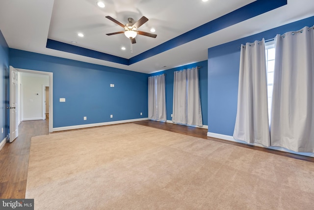 carpeted spare room with a raised ceiling and ceiling fan