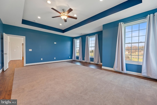 empty room with a raised ceiling, plenty of natural light, ceiling fan, and dark colored carpet