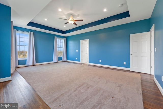 unfurnished room featuring dark colored carpet, a tray ceiling, and ceiling fan