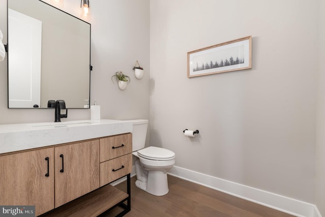 half bath with baseboards, toilet, wood finished floors, and vanity