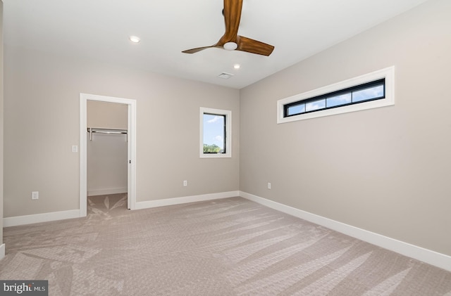 unfurnished bedroom featuring baseboards, recessed lighting, ceiling fan, light carpet, and a walk in closet