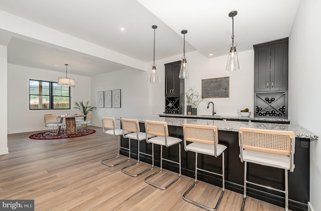 kitchen with light wood finished floors, baseboards, light stone countertops, a breakfast bar area, and hanging light fixtures