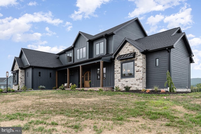 modern farmhouse featuring a porch, stone siding, roof with shingles, and board and batten siding