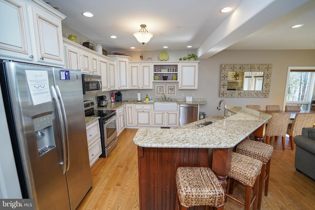 kitchen with light stone counters, light hardwood / wood-style floors, sink, hanging light fixtures, and stainless steel appliances