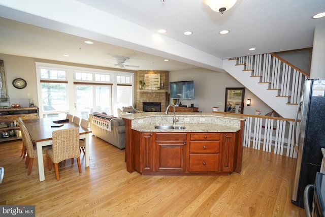 kitchen featuring ceiling fan, sink, stainless steel refrigerator, a large fireplace, and light hardwood / wood-style floors