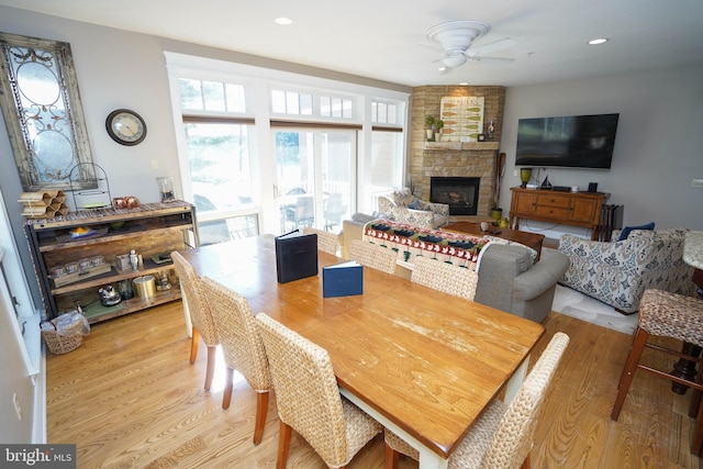 dining area with light hardwood / wood-style floors, ceiling fan, and a stone fireplace