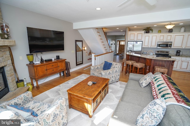 living room with ceiling fan, a stone fireplace, light hardwood / wood-style flooring, and sink