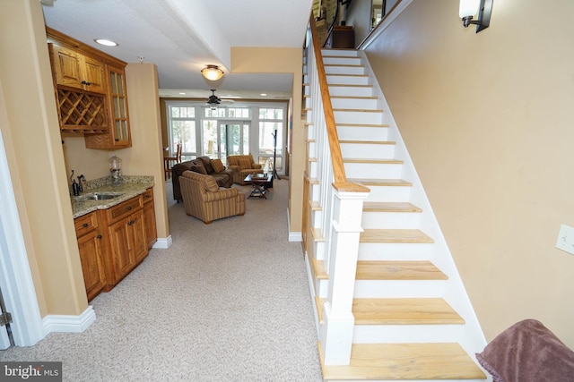 stairs with ceiling fan, sink, and carpet