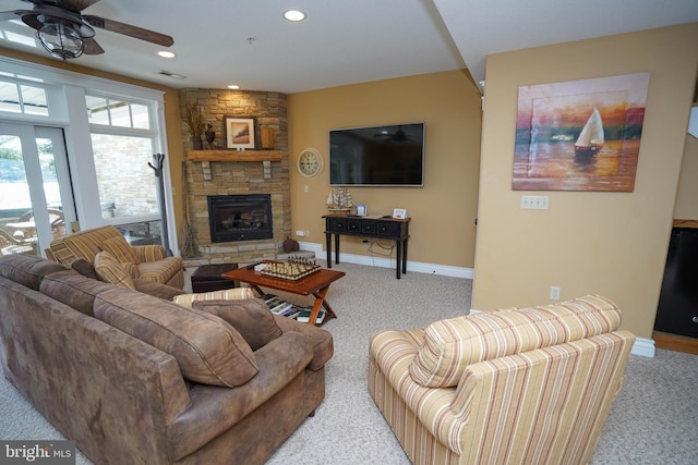 living room featuring ceiling fan, light colored carpet, and a stone fireplace