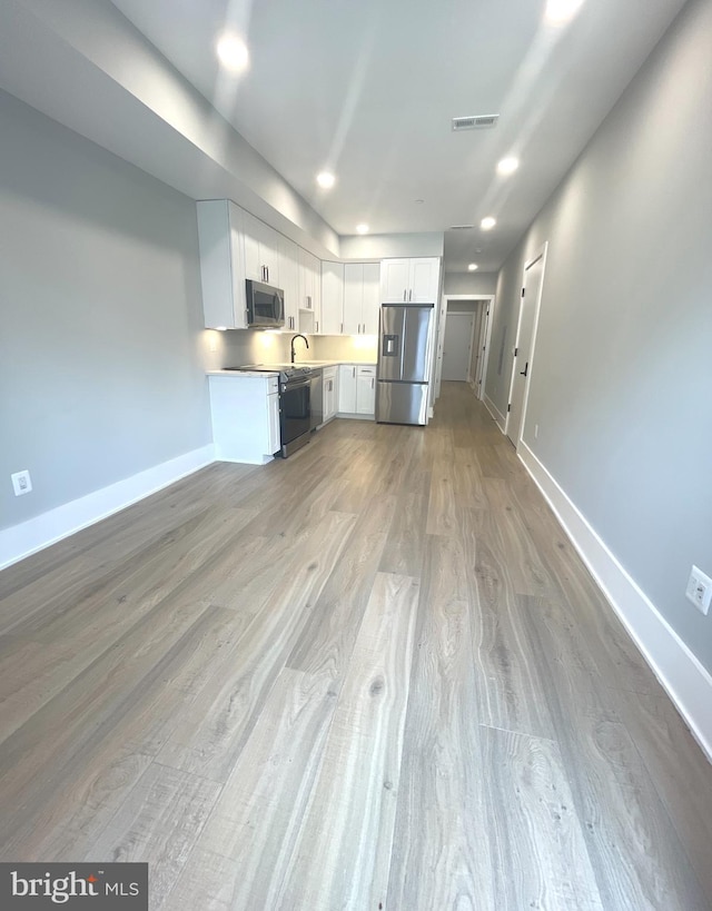 kitchen with sink, appliances with stainless steel finishes, hardwood / wood-style flooring, and white cabinetry