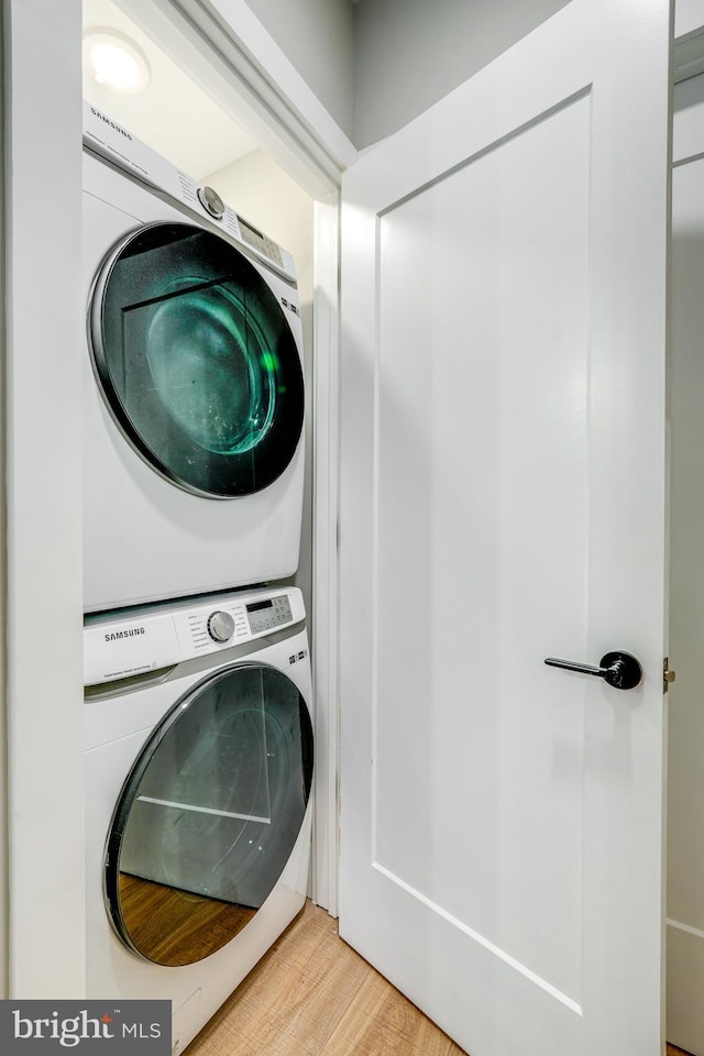 clothes washing area with light hardwood / wood-style flooring and stacked washer / drying machine