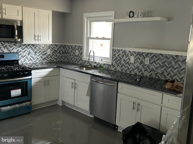 kitchen with appliances with stainless steel finishes, tasteful backsplash, white cabinets, dark tile floors, and sink