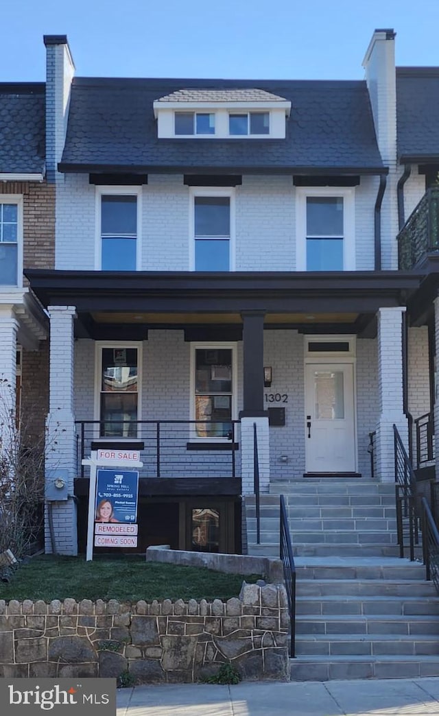 multi unit property featuring covered porch, brick siding, mansard roof, and stairway