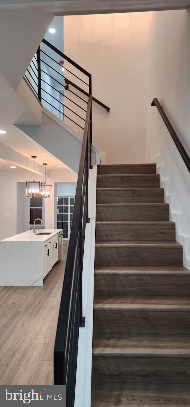 staircase with a chandelier, hardwood / wood-style flooring, and sink